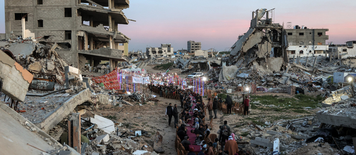 La gente se reúne junto a los escombros de los edificios destruidos para una reunión masiva para una comida comunitaria de ruptura del ayuno iftar en el segundo día del mes sagrado musulmán del Ramadán en el área de al-Dahduh en el distrito de Tal al-Hawa de la ciudad de Gaza e
