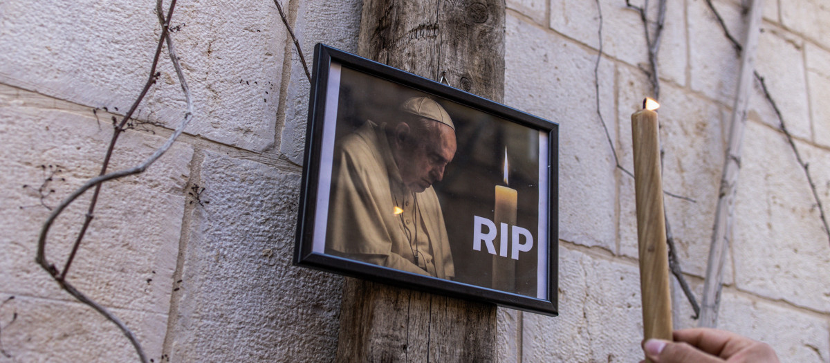 Un hombre enciende una vela junto a una foto del Papa Francisco en la Ciudad Vieja de Jerusalén