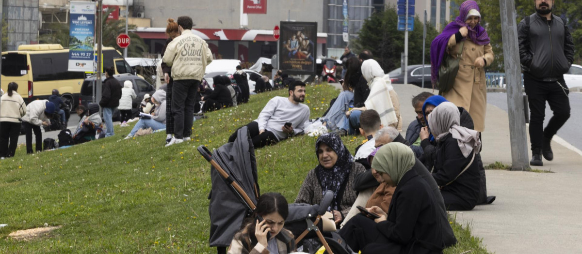 Personas con sus pertenencias sentadas en un parque tras un potente terremoto en Estambul