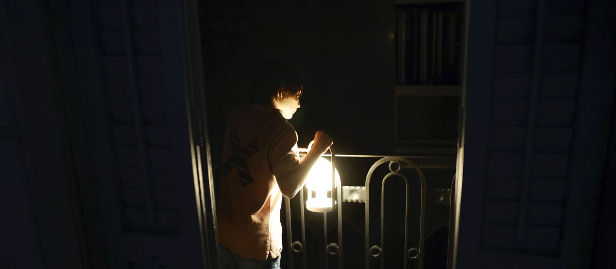 Un niño con una lámpara mira desde el balcón la calle todavía a oscuras esta madrugada en el centro de Barcelona durante el corte de suministro eléctrico