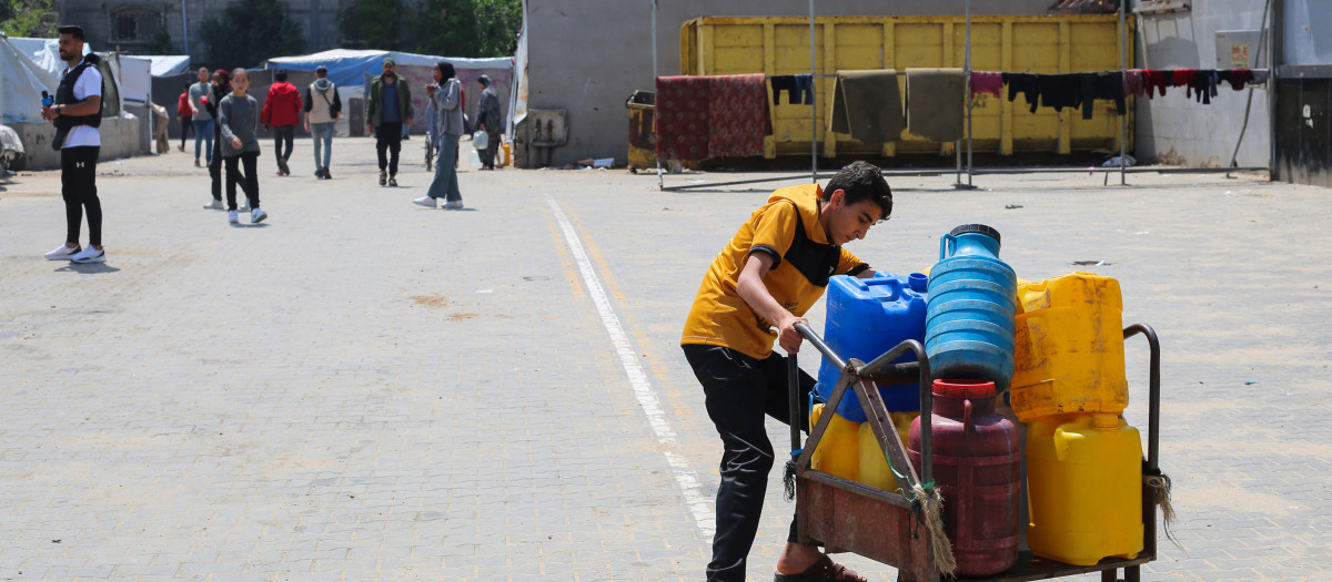 Un joven palestino lucha por transportar un carro lleno de contenedores de agua en un punto de distribución del campo de refugiados de Nuseirat