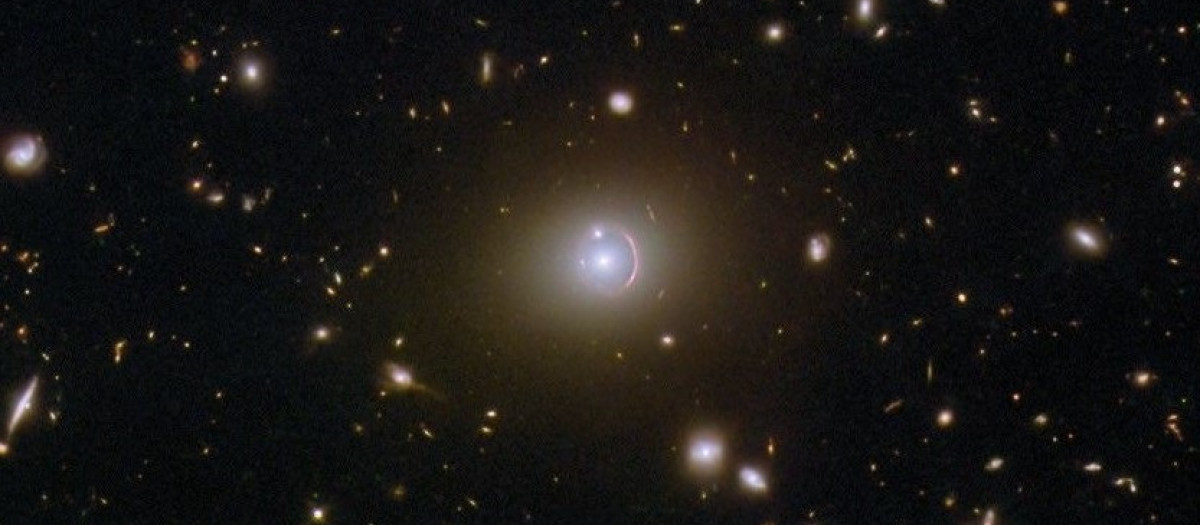 Esta imagen del telescopio espacial Hubble de la NASA/ESA muestra la galaxia remota HerS 020941.1+001557, que aparece como un arco rojo que rodea parcialmente una galaxia elíptica en primer plano