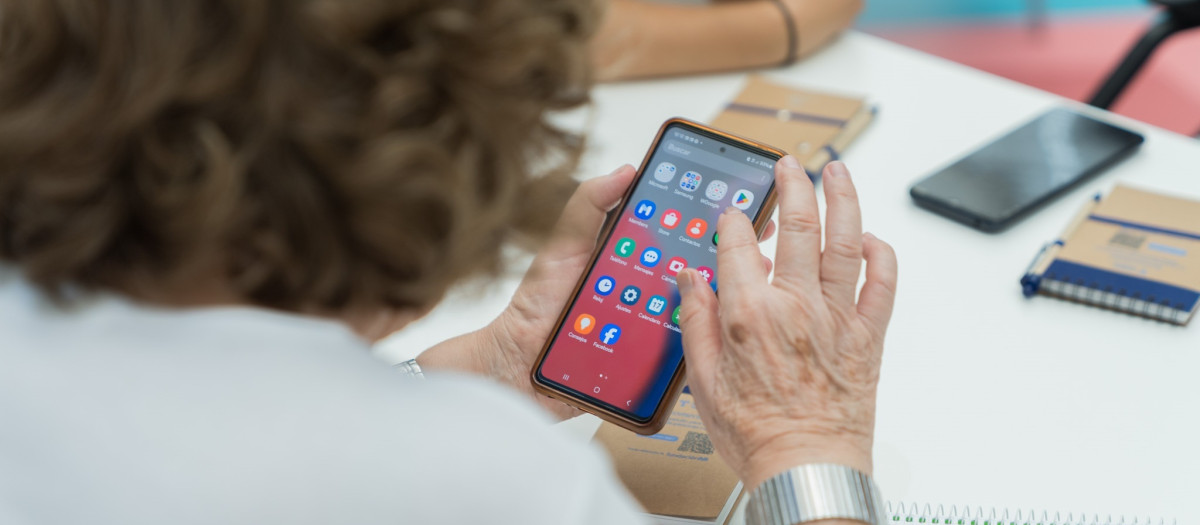 Una persona sostiene un teléfono móvil durante un curso de alfabetizacióin digital para personas mayores.
