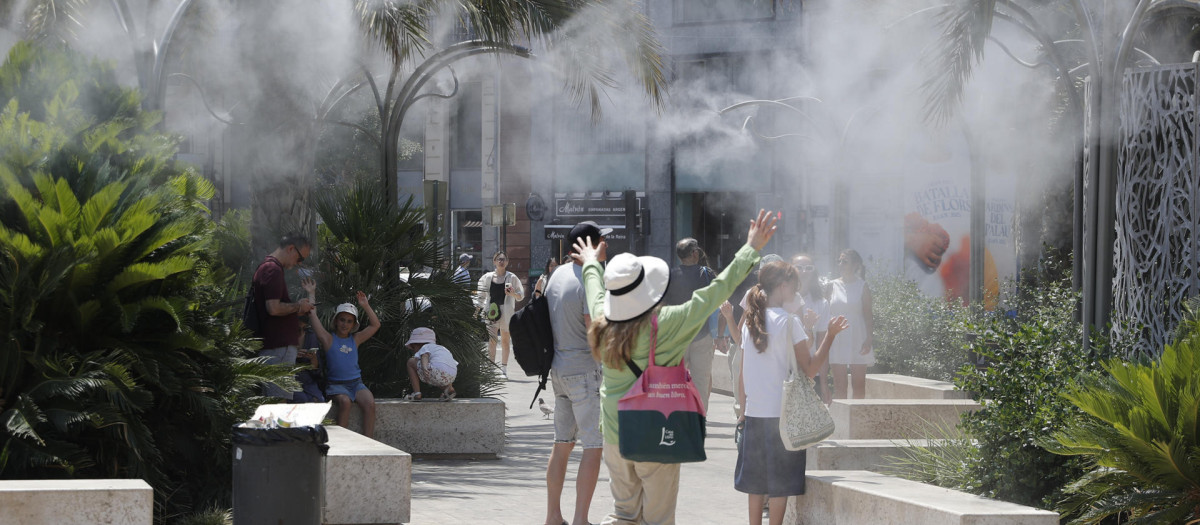 Varios turistas tratan de mitigar el calor bajo una nube de agua vaporizada en la plaza de la Reina de Valencia