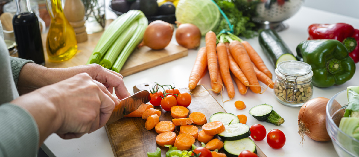 Primer plano de las manos de la mujer cortando zanahorias orgánicas frescas en la encimera de la cocina
