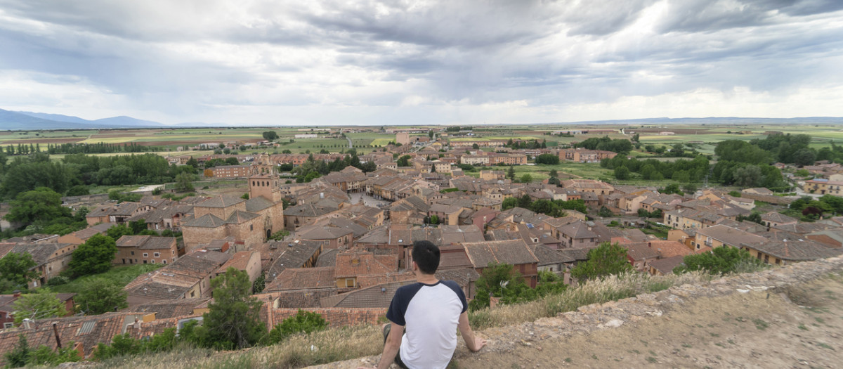 Joven sentado viendo pasar la vida mientras observa el pueblo medieval de Ayllón.