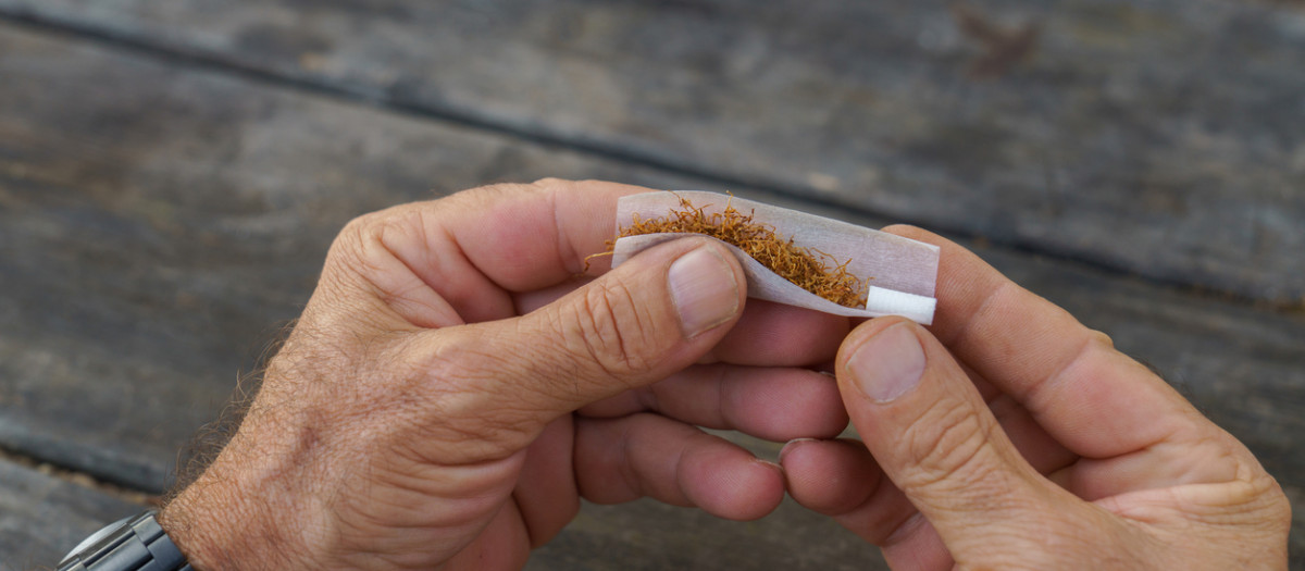 Una persona enrolla un cigarrillo sobre una mesa de madera