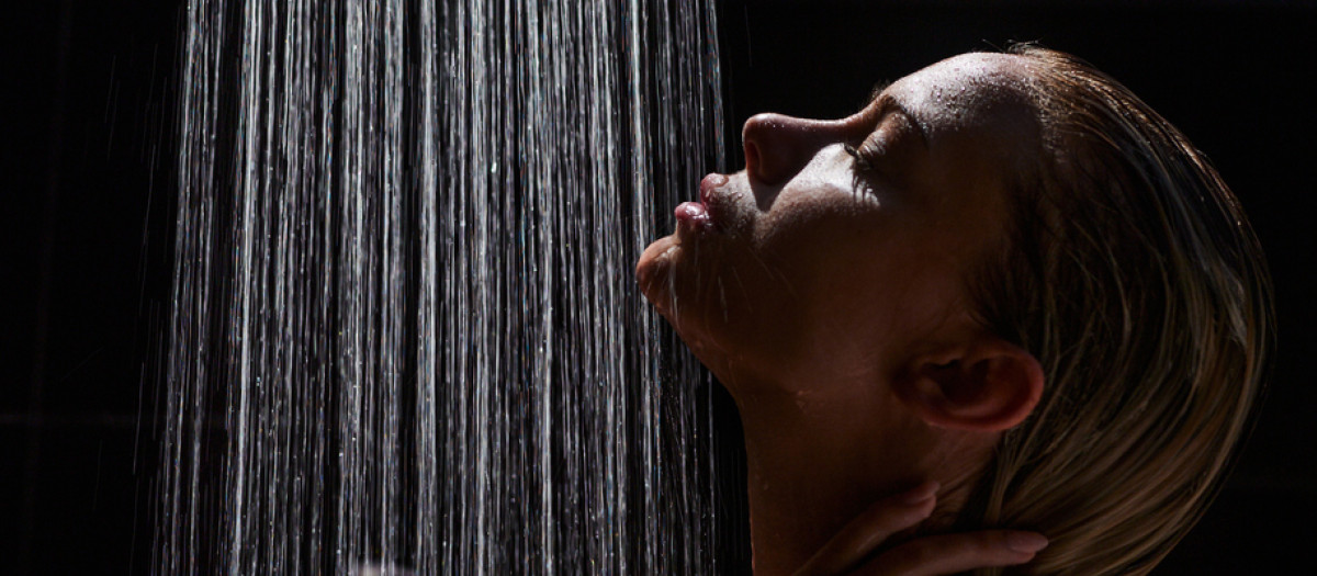 Profile view of carefree woman under the shower in the dark.