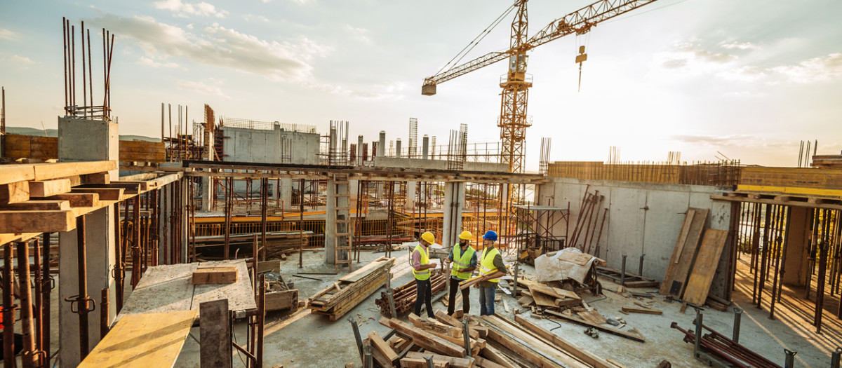 Construction industry concept - architects and engineers discussing work progress between concrete walls, scaffolds and cranes.