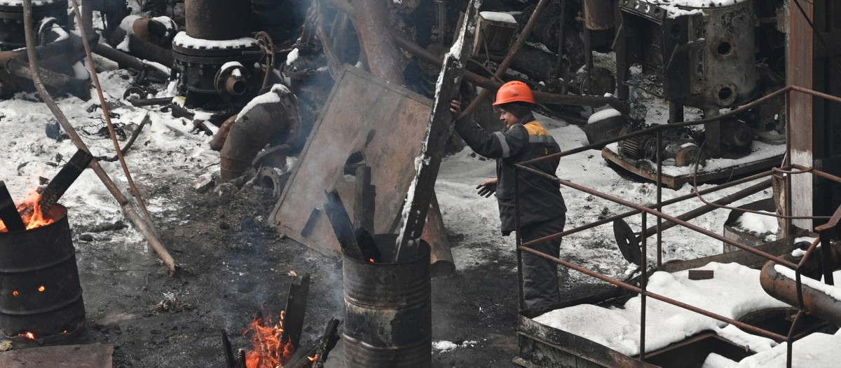 Un trabajador del sistema energético ucraniano se calienta en un barril con fuego en una de las plantas bombardeadas por Rusia esta madrugada