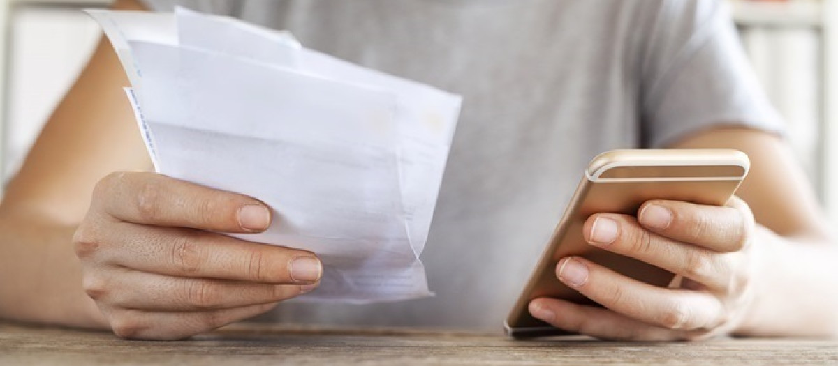 Persona sujeta un teléfono y una factura