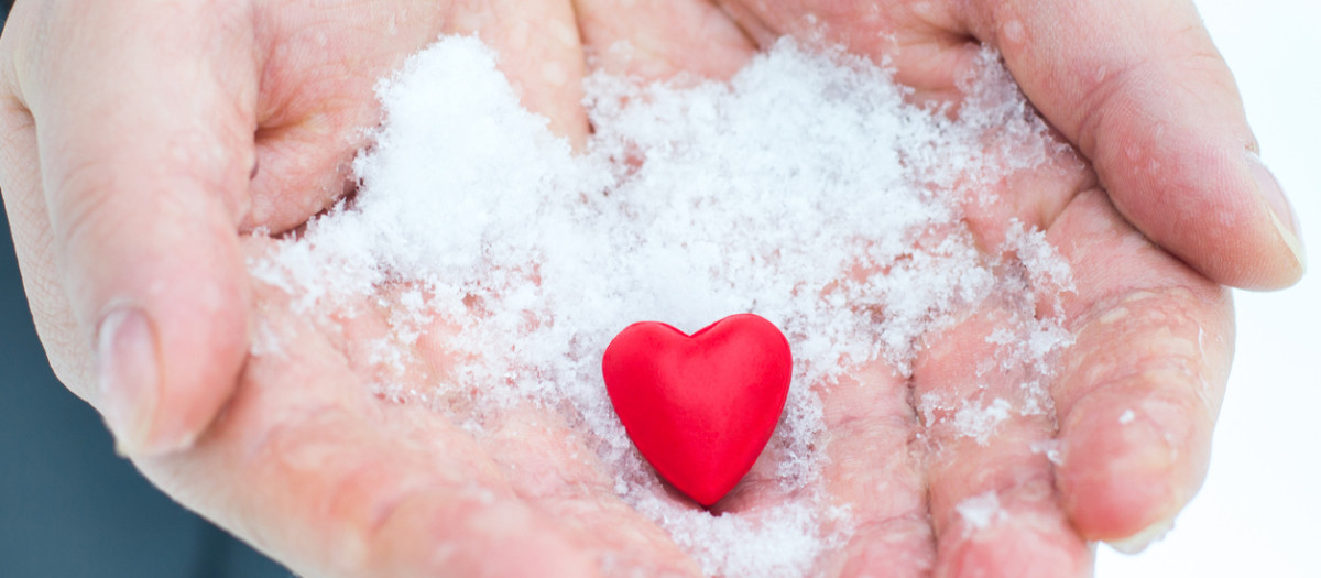 Hands giving a red heart in the snow, Valentine's Day, the theme of donation
