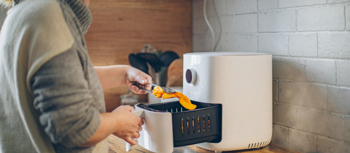 Mujer cocinando gajos de patata en una freidora de aire