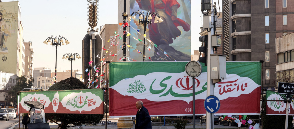 Pancartas con los colores de la bandera iraní adornan una rotonda mientras un hombre pasa por la capital iraní, Teherán