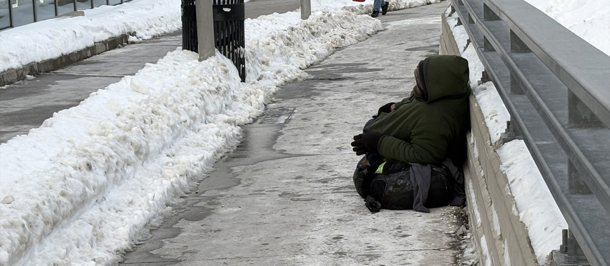 Un hombre sin hogar se sienta en el suelo, rodeado de nieve, frente a la terminal del ferry de Staten Island
