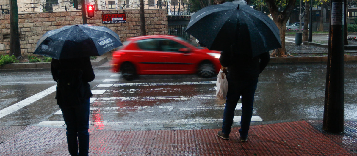Unos viandantes caminan con fuertes rachas de viento y lluvia en una calle de Almería