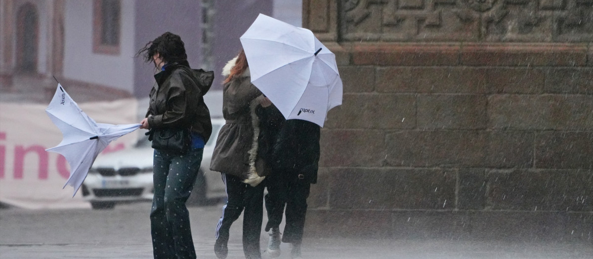 Varias personas intentan sujetar sus paraguas en Santiago de Compostela, La Coruña