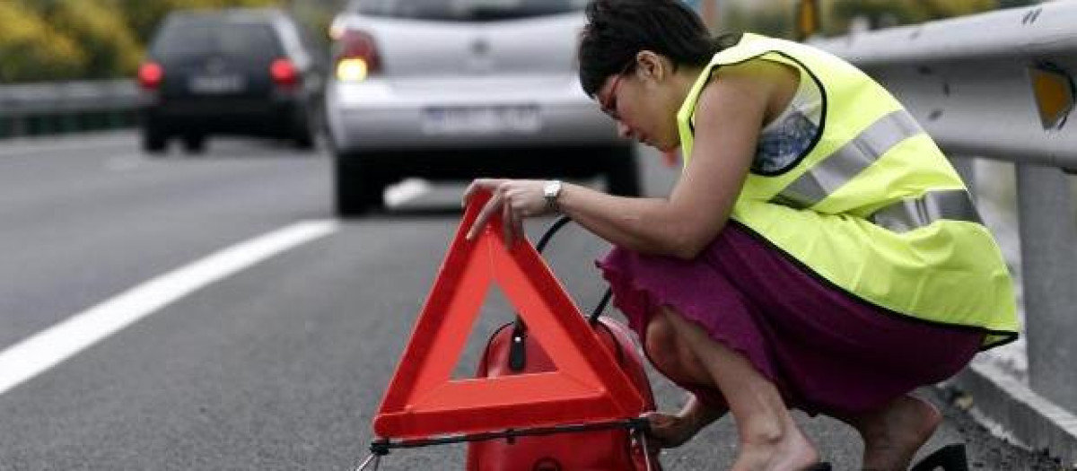 Una conductor coloca los triángulos de emergencia con el chaleco puesto