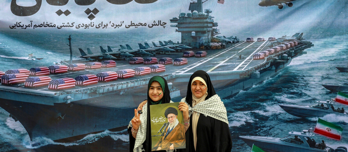 Mujeres posan con un cartel que representa al líder supremo de Irán, el ayatolá Alí Jamenei,  frente a una pancarta que representa un portaaviones de la Marina de los EE. UU.