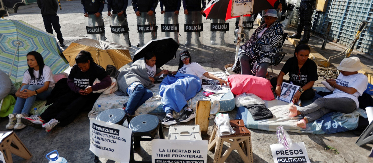 Relatives of political prisoners protest in front of a line of policemen outside the Bolivarian National Police (PNB) Zona 7 prison with a sign reading "In Venezuela, re-victimization and injustice have beEn normalized", "Freedom has no boundaries. Demand it with us" and "Political prisoners, neither forgetting nor silence, justice now!" in Caracas on February 13, 2026. Venezuelan lawmakers on Thursday postponed the adoption of a landmark amnesty bill designed to end the use of courts to crack down on dissent after failing to reach an agreement on how to apply it. (Photo by Pedro MATTEY / AFP)
