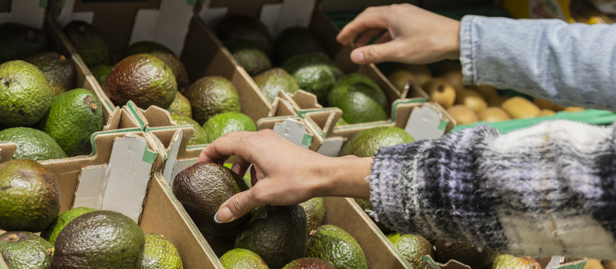 Una mujer eligiendo aguacate en el supermercado