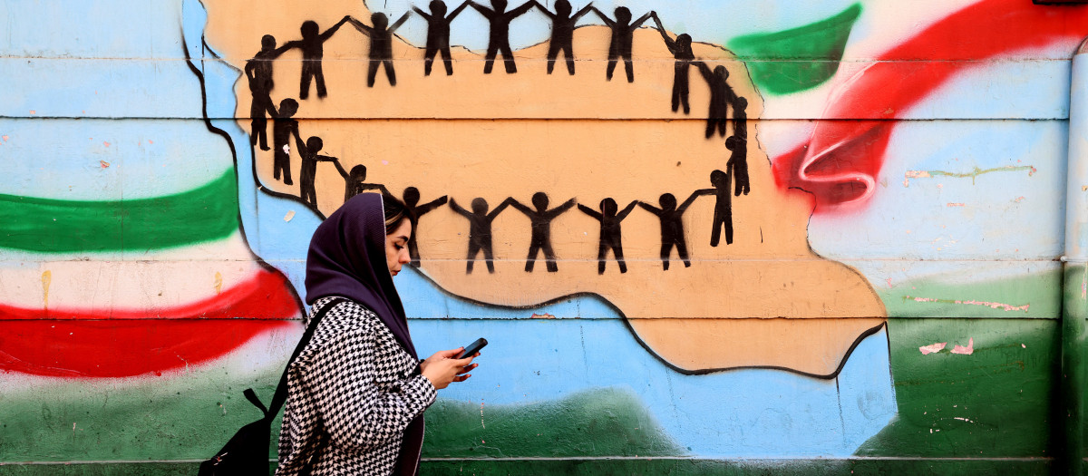 Una mujer pasa junto a la bandera y el mapa de Irán pintados en una pared en Teherán