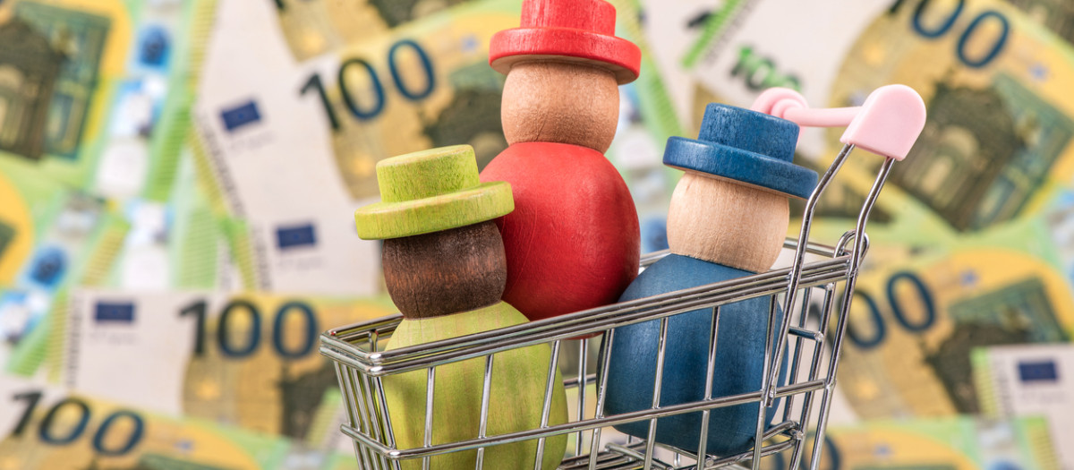 Personas de madera en un carrito de la compra, sobre un fondo con dinero