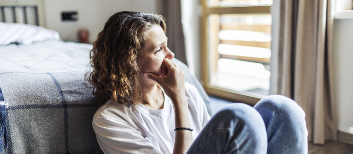 Young adult woman with depression sitting at home alone