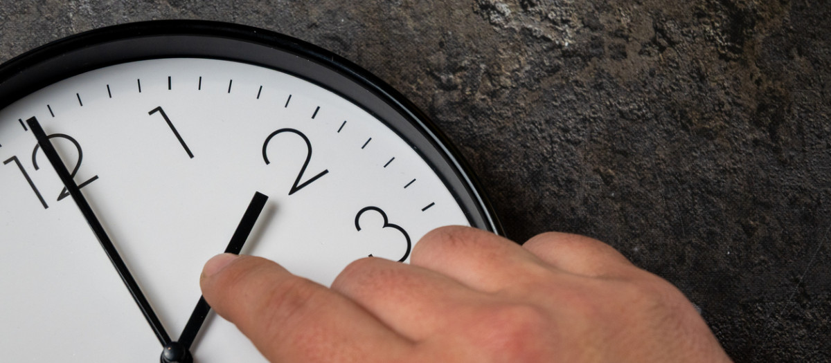 Close-up of a human hand adjusting a wall clock to represent daylight saving time change. The image symbolizes time adjustment, seasonal time shift, modern lifestyle, work schedule changes and the impact of time regulation on daily life.