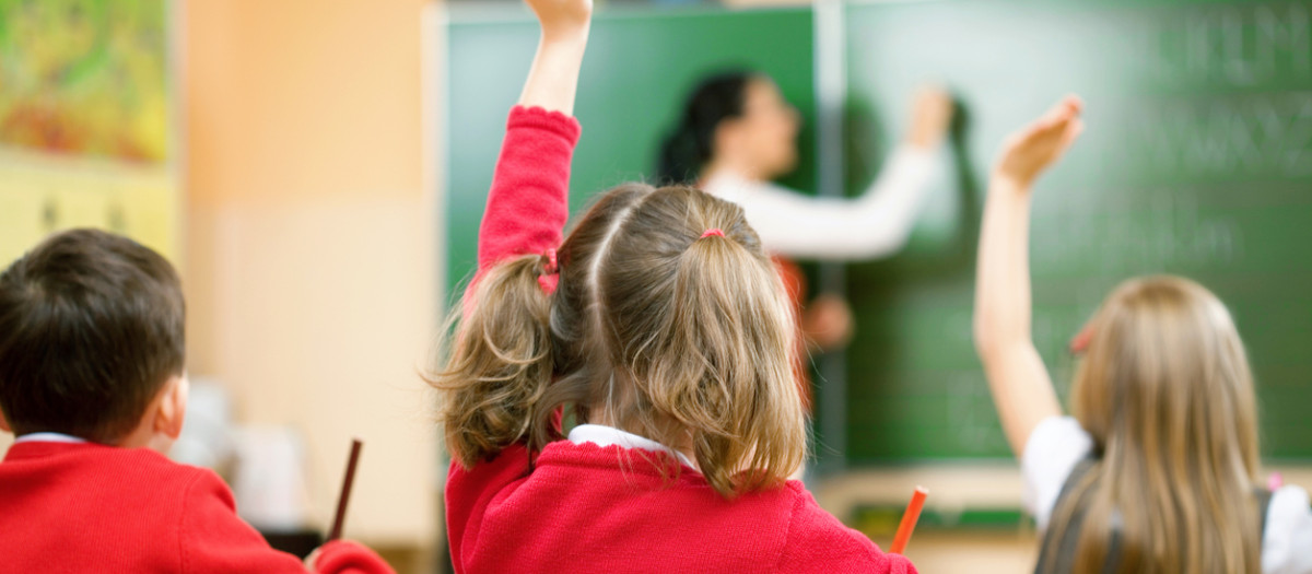Elementary school kids raising their hands in class to answer a teacher's question.