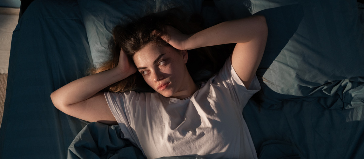 Restless people. Annoyed, Stressed young woman suffering from insomnia, awake in bed at night with headache because of disturbed loud noise, unable sleep. Top view