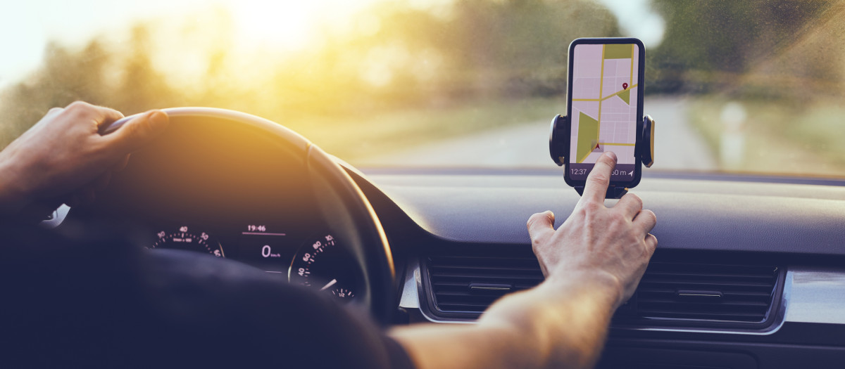 Driver using GPS navigation in mobile phone while driving car at sunset