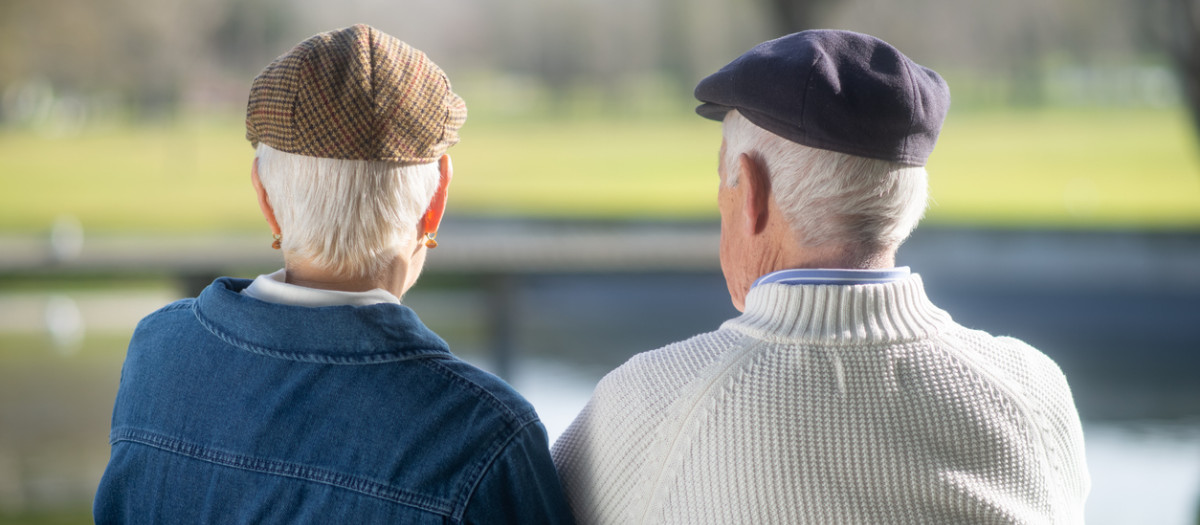 Back view of aged couple spending week end in park. Grey-haired husband and wife resting on bench outdoors, dreaming talking of life, looking far. Happiness, healthy lifestyle of aged people concept