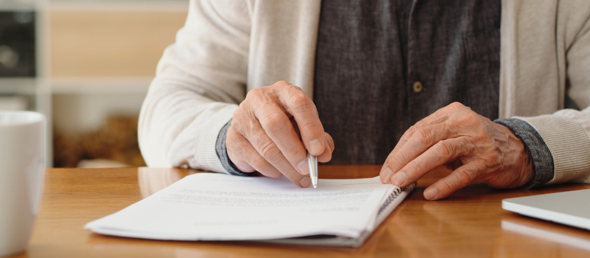 Hands of senior retirement woman writing a finance savings budget plan on paper or legal trust fund for after her funeral. Elderly person apply for pension or government financial support and help