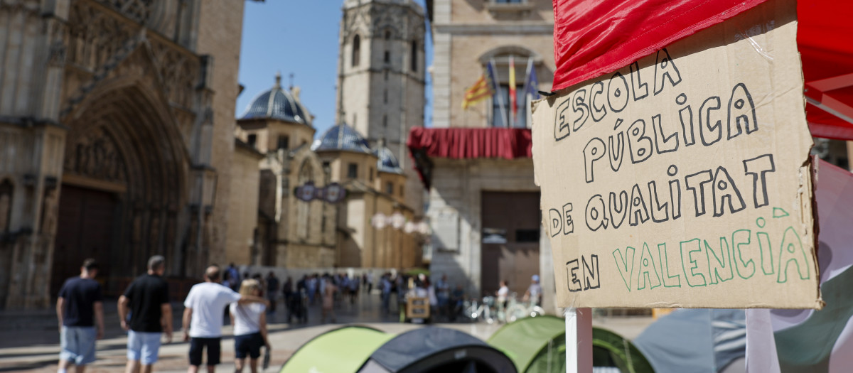 Imagen de un cartel en la acampada ilegal de docentes en la plaza de la Virgen de Valencia.