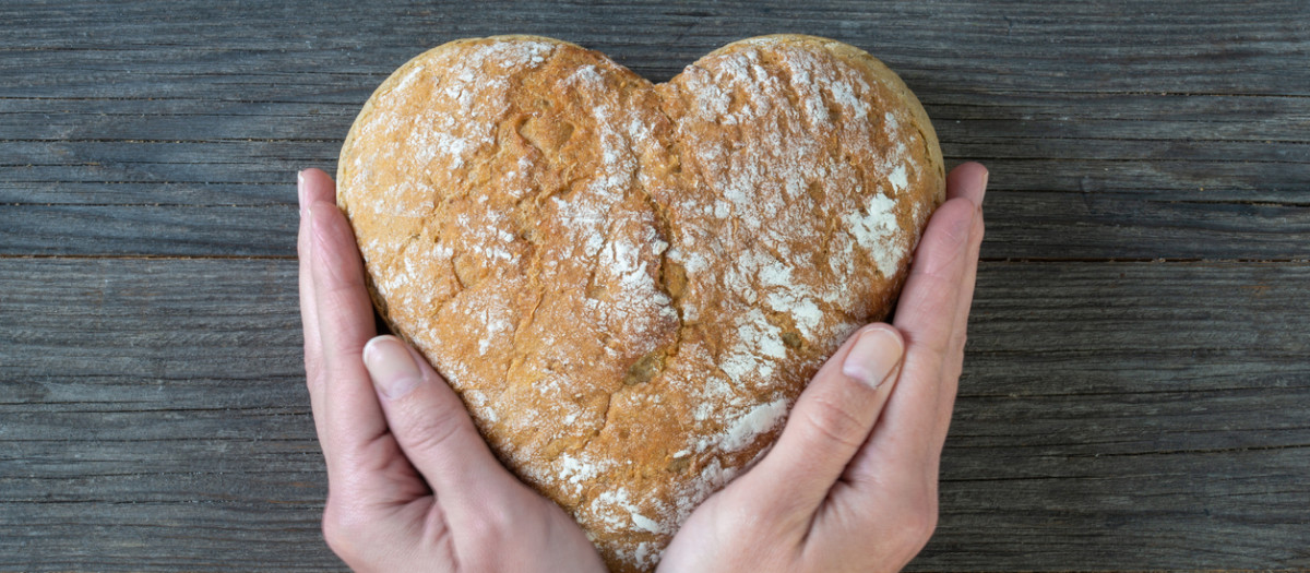 Unas manos sosteniendo un pan con forma de corazón, alimento esencial en toda dieta