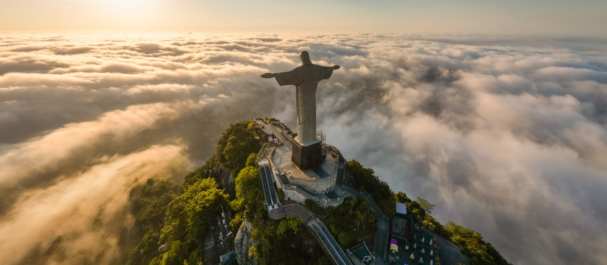 Rio de Janeiro, Brazil - April 11, 2024: Dramatic view of Christ the Redeemer statue on top of the Corcovado mountain above clouds during sunrise.