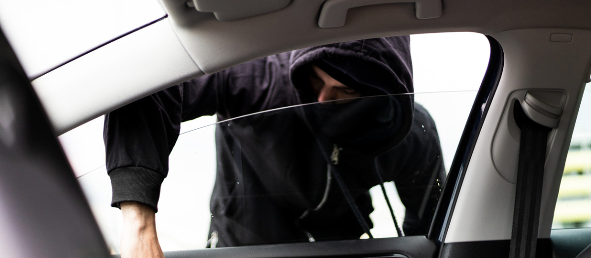Ladrón encapuchado robando en un coche