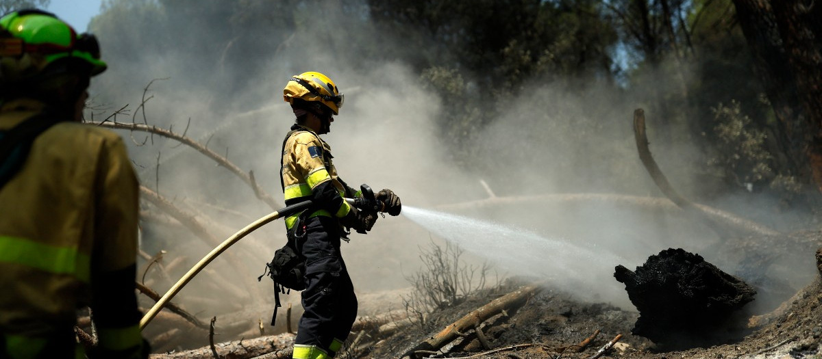 Bomberos rocían agua sobre el terreno para evitar que el fuego se reavive tras lograrse controlar un incendio cerca de La Adrada