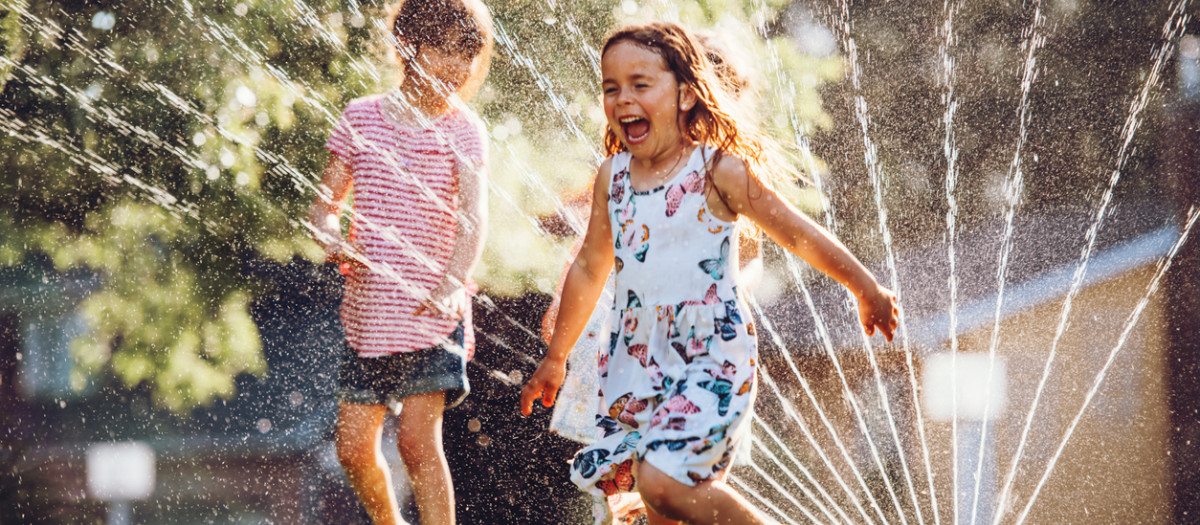 Unos niños juegan con el agua de un aspersor