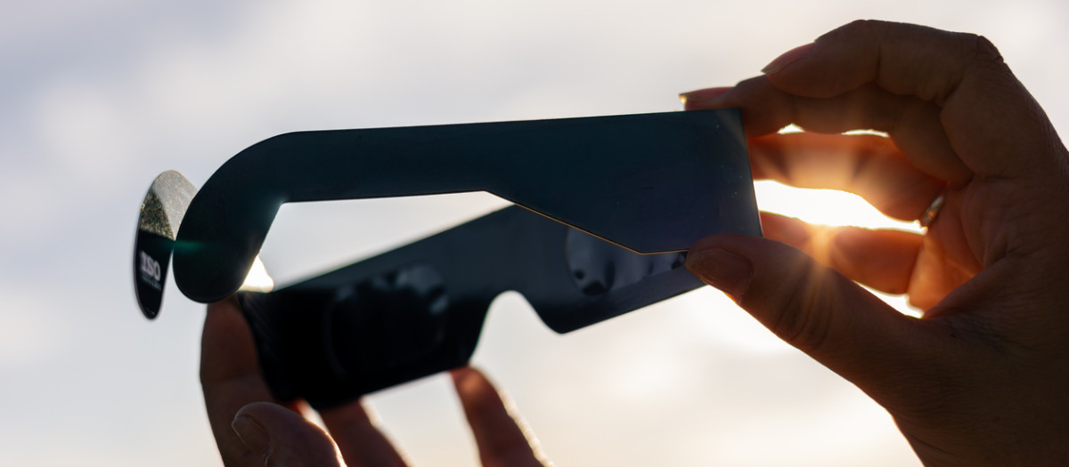 Person holding paper solar eclipse glasses, blocking the sun's direct rays for safe viewing during an astronomical event