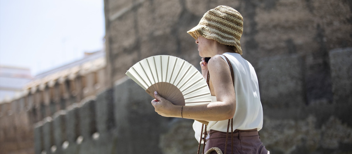 Una mujer se protege del sol con sombrero y abanico