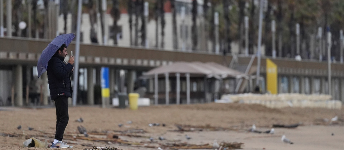 Vecinos de Barcelona pasean bajo la lluvia en la playa de la Barceloneta