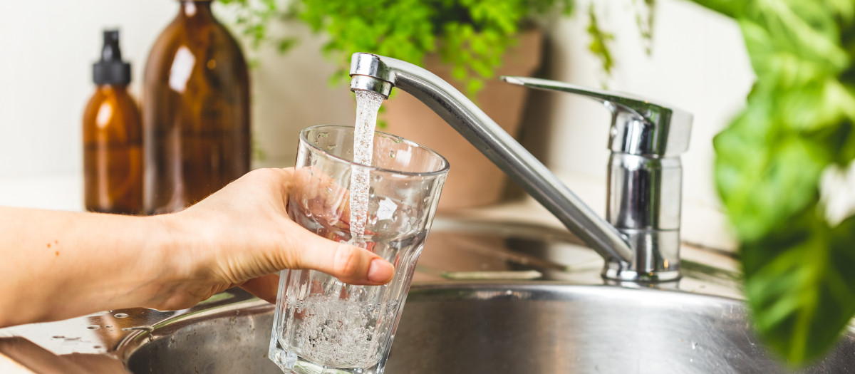 Female hand holding a glass and pouring it with tap water in the kitchen at home. Stay hydrated and filtering water concept. World water day