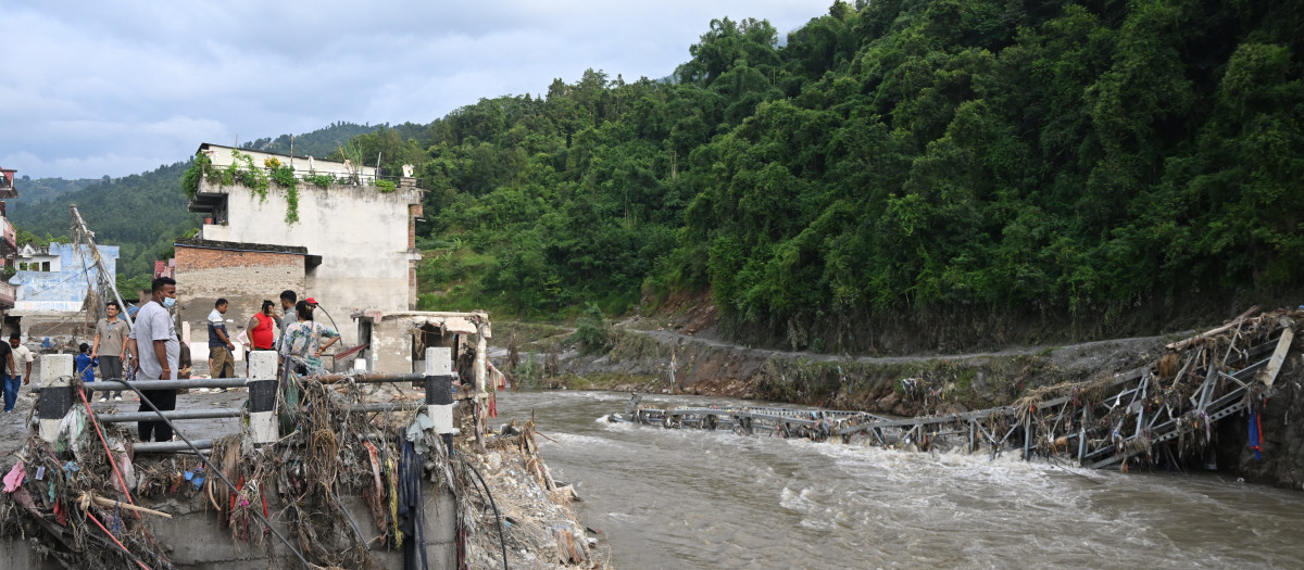 Unas personas permanecen cerca de un puente colapsado tras unas inundaciones repentinas en Devighat, en el distrito nepalí de Nuwakot