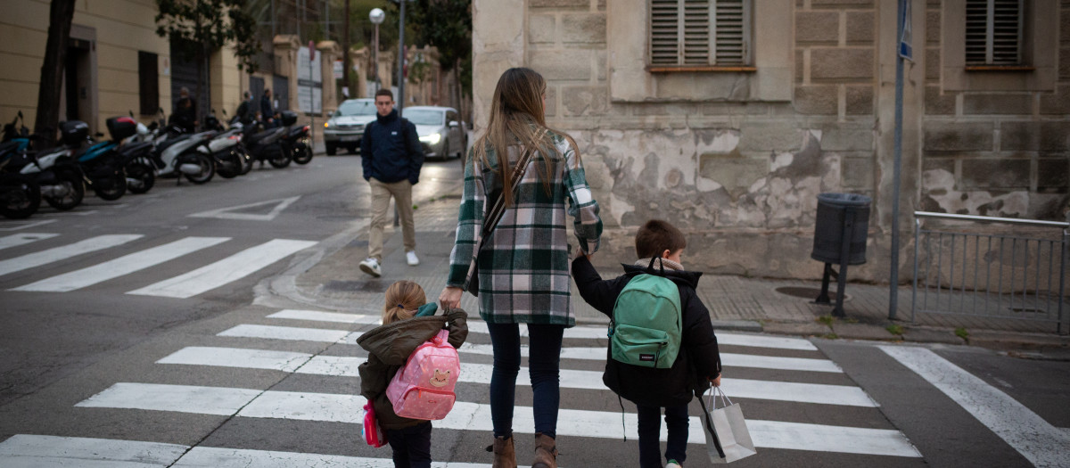 Dos niñas de la mano con una mujer a su llegada al primer día de clase presencia