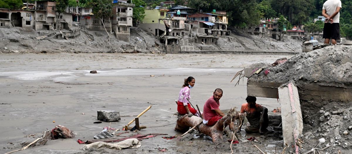 Unos residentes se sientan junto a los escombros mientras recuperan sus pertenencias tras unas inundaciones repentinas en Devighat