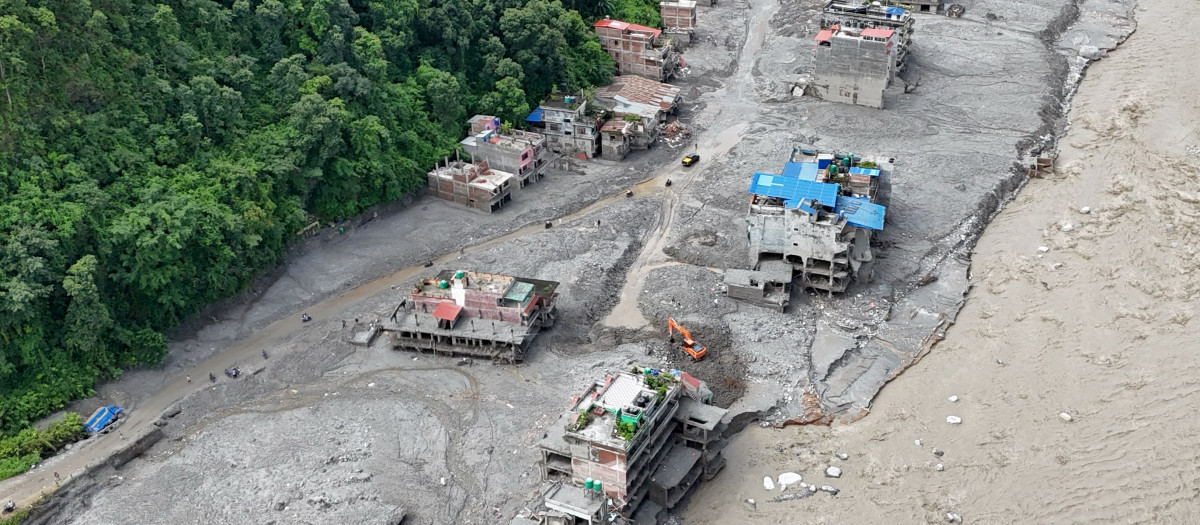 Una vista aérea muestra un torrente de agua fangosa que avanza con fuerza junto a las viviendas y a través del río Trishuli