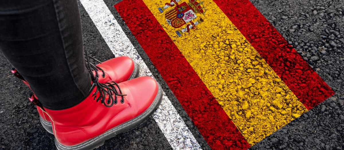 a woman with a boots standing on asphalt next to flag of Spain and border
