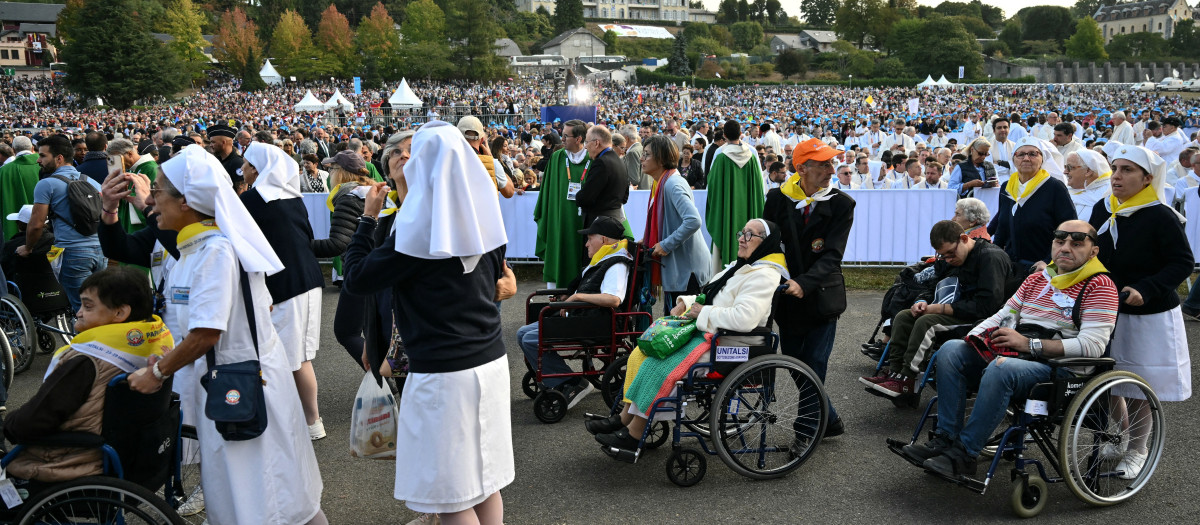 Unos voluntarios ayudan y empujan a los fieles en silla de ruedas hacia la pradera del Santuario de Nuestra Señora de Lourdes para asistir a la Santa Misa celebrada por el León XIV